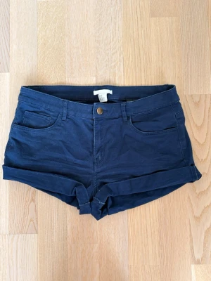 Mörkblå shorts från H&M - Snygga mörkblå shorts från H&M med upprullade benslut och klassisk femficksdesign. De har knapp och dragkedja framtill samt bälteshällor. Perfekta för varma dagar och enkla att matcha med olika stilar.