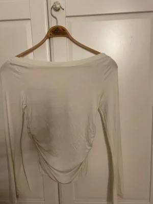 Vit långärmad topp från Gina Tricot - Säljer en stilren vit långärmad topp från Gina Tricot. Toppen har en bred, något båtformad urringning och är tillverkad i ett mjukt, stretchigt material som sitter snyggt på kroppen. Perfekt att matcha med jeans eller kjol.