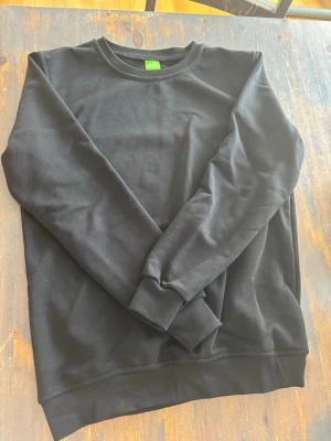 Svart sweatshirt från BOSS - Svart sweatshirt från BOSS med rund halsringning och diskret broderad logga på bröstet. Tröjan har långa ärmar och ribbade muddar vid ärmslut och nederkant. Perfekt för en stilren och avslappnad look.