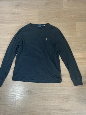 Mörkblå långärmad tröja Polo Ralph Lauren - Klassisk mörkblå långärmad tröja från Polo Ralph Lauren med rund halsringning och den ikoniska broderade loggan på bröstet. Tillverkad i mjukt bomullsmaterial som är skönt mot huden. Perfekt till jeans eller chinos för en clean look.