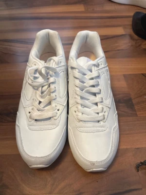 Helvita chunky sneakers - Säljer ett par helvita chunky sneakers med klassisk siluett och tjock sula. Skorna har vita snören och ovandel i syntetmaterial med meshdetaljer. Perfekta för dig som gillar en clean och sportig look. Aldrig användt