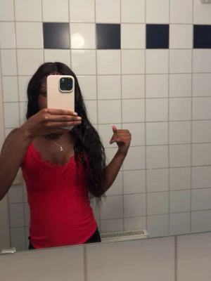 Röd spetsdetaljerad linnetopp - Snygg röd linnetopp med tunna axelband och spetsdetaljer längs urringningen. Toppen är figurnära och passar perfekt till jeans eller kjol för en trendig look.