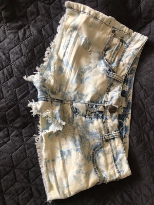Blåvit batikmönstrafe slitna jeansshorts Freestyle - Snygga blåvita jeansshorts från Freestyle Revolution med slitna detaljer och fransig kant. Shortsen har klassisk femficksmodell och knäppning fram. Materialet är en mix av bomull, polyester och lite spandex för stretch. Väl använda men har mer kvar att ge, så snygga!