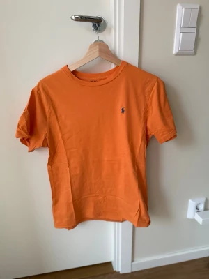 Orange t-shirt Ralph Lauren - Snygg orange t-shirt från Ralph Lauren med klassisk passform och korta ärmar. 