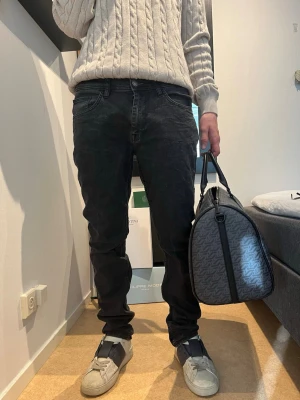 Svarta slim fit jeans från Replay - Säljer ett par svarta slim fit jeans från Replay med klassisk femficksmodell och låg midja. Jeansen har en snygg tvättad look och är tillverkade i mjukt denimtyg med lite stretch för extra komfort. Perfekta för en avslappnad och trendig stil. Modellen är 182 75kg