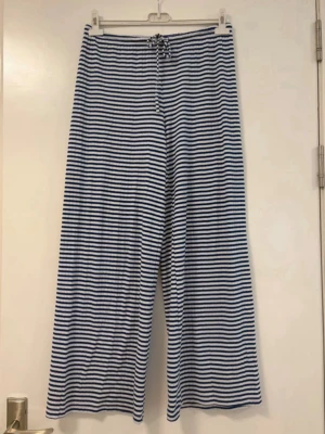 Randiga vida loungewear-byxor - Mysiga loungewear-byxor med blå och vita horisontella ränder. Byxorna har en avslappnad, vid passform och dragsko i midjan för extra komfort. Perfekta för chill dagar hemma eller när du vill vara bekväm.