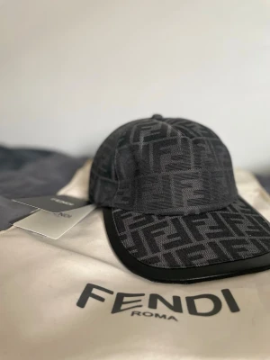 Svart keps med Fendi-logga - Säljer en svart keps från Fendi med det klassiska FF-monogrammet över hela kepsen. Kepsen har böjd skärm och är tillverkad i ett tygmaterial med exklusiv känsla. Perfekt för dig som vill ha en stilren accessoar med lyxig touch.