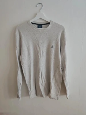 Ljusgrå tröja från Ralph Lauren - Säljer en stilren ljusgrå tröja från Ralph Lauren med rund halsringning och den klassiska broderade loggan på bröstet. Tröjan har långa ärmar och är tillverkad i mjukt material som passar perfekt till jeans eller chinos.
