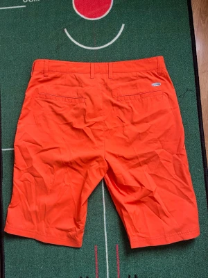 Orange shorts från Callaway - Snygga orange shorts från Callaway med klassisk passform. Shortsen har två bakfickor och bälteshällor i midjan. Perfekta för sommardagar och golfbanan. Tillverkade i ett lätt och bekvämt material. Stork i L 