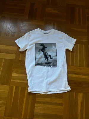 Vit t-shirt med cowboymotiv Julian Vane - Vit t-shirt från Julian Vane med ett stort svartvitt cowboymotiv på framsidan och texten 'Julian Vane Stockholm' under bilden. Klassisk rund hals och korta ärmar, perfekt för dig som gillar coola prints och streetstyle.