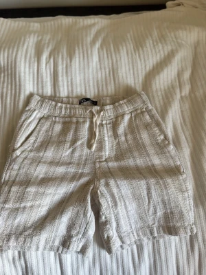 Beige shorts med snörning från Zara - Säljer ett par beige shorts från Zara med snörning i midjan och fickor både fram och bak. De är tillverkade i ett strukturerat bomullstyg och har en avslappnad passform som passar perfekt till sommaren. Säljer pga försmå