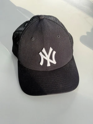 Svart New Era Yankees keps - Snygg svart keps från New Era med klassisk New York Yankees-logga broderad i vitt framtill. Kepsen har böjd skärm och mesh-paneler på sidorna och bak för extra ventilation. Perfekt för dig som gillar sportig streetstyle.