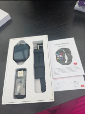 Svart smartklocka med silikonarmband - Stilren svart smartklocka med fyrkantig display och svart silikonarmband. Klockan har touchskärm och levereras med laddkabel och användarmanual. Perfekt för att hålla koll på notiser, träning och hälsa direkt på handleden.