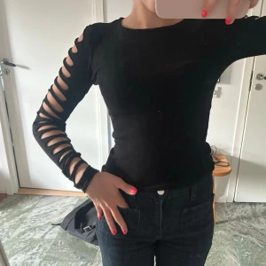 Svart långärmad topp med cut-outs - Svart långärmad topp med tight passform och cut-outs längs båda ärmarna. Super cool!