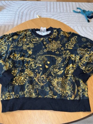 Versace tröja svart med guld - Äkta svart Versace sweatshirt med guld mönster, XXL men passar XL.