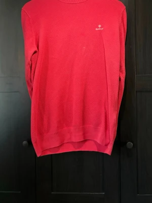 Röd tröja från Gant - Röd stickad tröja från Gant med diskret logga broderad på bröstet. Tröjan har rund halsringning, ribbade muddar och nederkant. Perfekt för dig som gillar klassisk och stilren design.