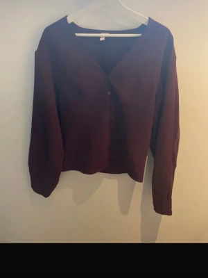 Vinröd blus med knappar - Stilren vinröd blus med v-ringning och knäppning framtill. storlek m men sitter som s Blusen har långa ärmar och är tillverkad i ett tunt, mjukt tyg som ger ett snyggt fall. lite tajtare vid midjan Perfekt att matcha med jeans eller kjol för en trendig look.