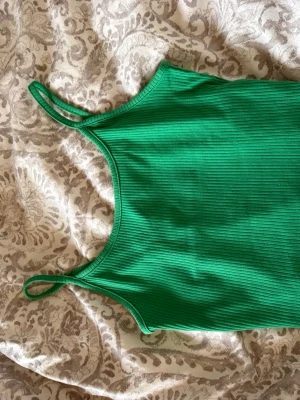Grön ribbad linnetopp med smala band - Cool grön linnetopp med smala axelband och ribbad struktur. Perfekt att matcha med jeans eller shorts för en avslappnad look. Toppens form är croppad och materialet känns mjukt och stretchigt.