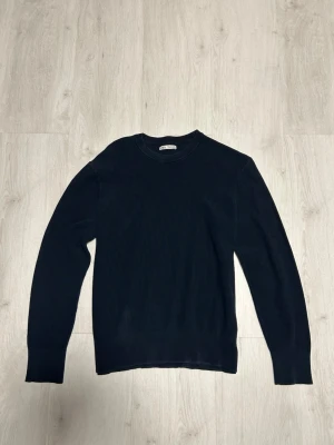Mörkblå stickad tröja från Zara - Mörkblå stickad tröja från Zara med rund halsringning och diskret ribbad struktur. Tröjan har långa ärmar och en klassisk, enkel design som passar till det mesta. Perfekt för lager på lager och stilrena outfits. Storlek M.