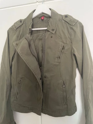 Vårjacka  - Snygg olivgrön/ khaki färgad jacka från H&M dragkedjor på bröstet och sidorna och många detaljer! Jackan har axelklaffmilitärinspirerad look som passar till det mesta. storlek 36. Perfekt nu inför våren! Skriv om du har några frågor!🌟