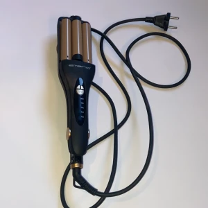 Vågtång från Emerio svart/guld - Säljer en vågtång från Emerio med svart handtag och guldfärgade värmeplattor. Tången har tre cylindriska värmeelement och en tydlig temperaturinställning på handtaget. Utrustad med lång svart sladd och EU-kontakt. Perfekt för att fixa snygga beach waves. Kommer från jultidningen när jag sålde.