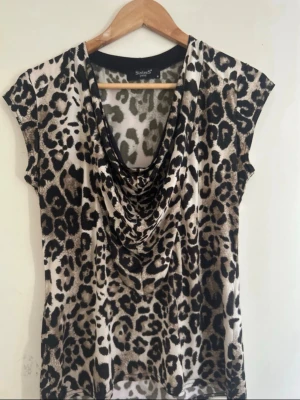 Leopardmönstrad topp från Sisters Point - Snygg leopardmönstrad topp från Sisters Point med draperad ringning och korta ärmar. Tunn och mjuk polyester som känns skön mot huden. Perfekt för dig som vill sticka ut med ett djurmönster och en avslappnad men trendig look.