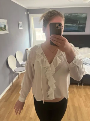 Vit blus med volang och knytband - Säljer en vit blus med långa ärmar, volangdetaljer längs ringningen och framtill samt knytband vid halsen💗