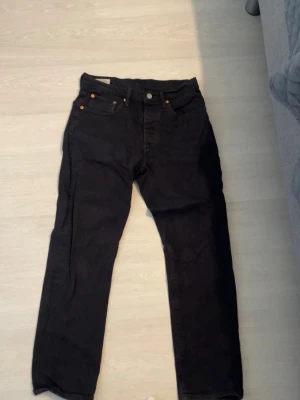 Levi's 501 svarta jeans - Klassiska svarta Levi's 501 jeans med rak passform och ikonisk läderpatch bak i midjan. Jeansen är tillverkade i bomull och har tidlös design som funkar till allt. Perfekta för dig som gillar en clean och enkel look.