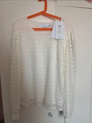 Vit spetsmönstrad blus från Vila - Säljer en vit långärmad tröja från Vila med snyggt spetsmönster och rund halsringning. Tröjan har en luftig och feminin look, perfekt för att lyfta vilken outfit som helst. Materialet är lätt och ger en elegant känsla.