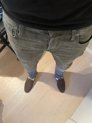 Grå slim fit jeans från Jack and Jones  - Säljer ett par grå slim fit jeans från Jack and Jones med klassisk femficksdesign och snygga detaljer på bakfickorna. Jeansen har en modern passform och är tillverkade i mjukt denim-material som är bekvämt att bära. W-31 L-32