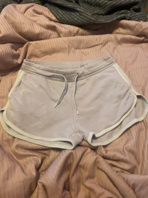 Ljuslila mjukisshorts med snörning - Säljer ett par ljuslila mjukisshorts med vita kanter och snörning i midjan från firefly jag tror de är ifrån Intersport men osäker tanken på att jag fick dom i present 2020. Shortsen har en sportig look och är perfekta för avslappnade dagar. Är perfekt att ha till stranden eller om man ska åka och bada på badhus även till att ha som pjamasshorts. Det är mjukt och skönt material för extra komfort.