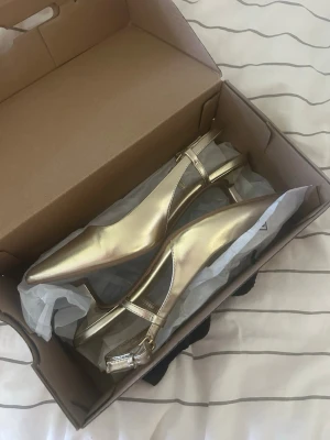 Guldiga klackskor - Guldiga klackskor som endast är använda en gång, ca 5 cm klack, ej smutsiga eller några flagor/fläckar på de. Köptes på Zalando från Call It Spring. Storlek 36, finns band runt hälen som går att spänna åt!