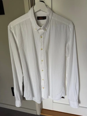Vit seersucker skjorta från Morris - Vit skjorta från Morris i bomull. Skjortan har lång ärm, knappar framtill och button-down krage. Perfekt till både jeans och chinos för en clean och stilren look.