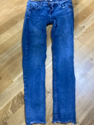 Blå skinny jeans med råa kanter - Säljer ett par blå skinny jeans med råa, avklippta benslut. Klassisk femficksmodell med normal midja och dragkedja. Jeansen har en snygg tvätt och är perfekta för en avslappnad look. Materialet är denim i bomull.