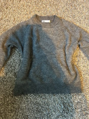 Mörkgrå stickad tröja från Zara - Mysig mörkgrå stickad tröja från Zara med rund halsringning och ribbade muddar vid ärmslut och nederkant. Perfekt för lager på lager och enkel att matcha med olika outfits. Klassisk och stilren design som passar till det mesta.