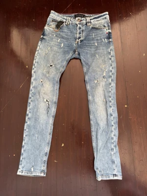 Ljusblå slitna jeans från Philipp Plein - Säljer ett par ljusblå skinny jeans från Philipp Plein med slitningar och distressed detaljer. Jeansen har fem fickor, silverfärgad D-ring framtill och logga på bakfickan. Storlek 31 i midjan.