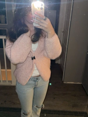 Ljusrosa fluffig kofta  - Supermjuk och fluffig ljusrosa kofta. Koftan har en avslappnad passform och långa ärmar, perfekt att slänga på sig över en t-shirt. Materialet ser ut att vara stickat och ger en mysig känsla.