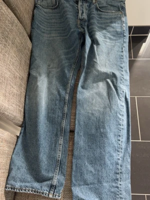 Blå raka jeans i klassisk modell - Säljer ett par ljusblå jeans med rak passform och hög midja. Jeansen har fem fickor och klassisk denimlook med subtila slitningar. Perfekta till en avslappnad stil och passar till det mesta. Materialet är kraftig bomullsdenim.