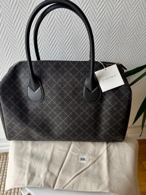 Ny By Malene Birger Weekendbag ”Lullu” - Dark Chocolate - Helt ny med tags och dustbag enligt bilder!  Färg: Dark Chocolate  ”Rymlig duffelväska med By Malene Birger signaturmönster. Väskan har dubbla handtag och en avtagbar, justerbar axelrem. Insidan är fodrad och har ett huvudfack samt en mindre ficka med dragkedja. Perfekt för resor eller som en större vardagsväska.”  Mått: 44*25cm  Nypris: 5095kr  Se gärna mina övriga annonser för bundlerabatter och samfrakt!