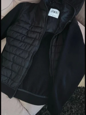 Svart pufferjacka med huva från ZARA - Svart pufferjacka från ZARA med huva och dragkedja framtill. Jackan har quiltade partier på framsidan och släta ärmar. Perfekt för dig som gillar en enkel men ändå trendig look.