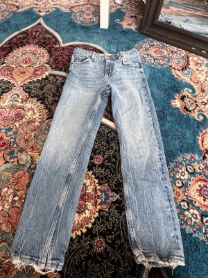 Ljusblå raka jeans från ZARA - Säljer ett par ljusblå raka jeans från ZARA med klassisk femficksmodell och hög midja. Jeansen har slitna detaljer och är tillverkade i bomull. Perfekta för en avslappnad och trendig look.