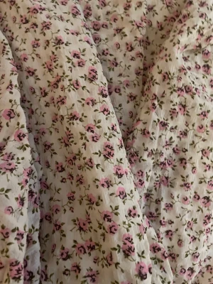 Blommig kortklänning med puffärm - Söt kortklänning med små rosa blommor på vit botten. Klänningen har puffiga trekvartsärmar och omlott över bysten. Perfekt för varma dagar och somriga tillfällen. Tillverkad i ett lätt och luftigt material. Priset kan diskuteras