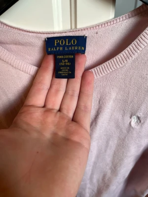 Ljusrosa stickad tröja Polo Ralph Lauren - Ljusrosa stickad tröja från Polo Ralph Lauren i mjuk pima cotton. Klassisk rund halsringning, långa ärmar och diskret broderad logga på bröstet. Perfekt för en chill och stilren look.