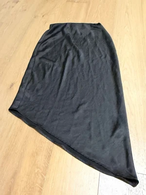 Svart asymmetrisk kjol från ONLY - Svart kjol från ONLY i storlek S med snygg asymmetrisk skärning. Kjolen är enkel och stilren, perfekt för dig som gillar minimalistisk design. Materialet känns mjukt och lätt, vilket gör den bekväm att bära hela dagen.