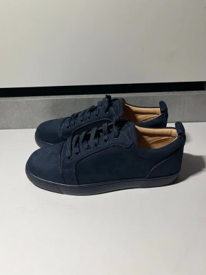 Mörkblå sneakers från Christian Louboutin - Snygga mörkblå sneakers i mocka från Christian Louboutin med klassisk röd sula och diskret logga. Skorna är helt nya, oanvända stilrena och snygga