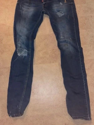 Jeans  - Säljer ett par blå jeans med slitningar och raka ben. Jeansen har klassisk femficksdesign och snygga detaljer med slitna partier på låren och knäna. Perfekta för en avslappnad och trendig look. Materialet är denim i bomull.