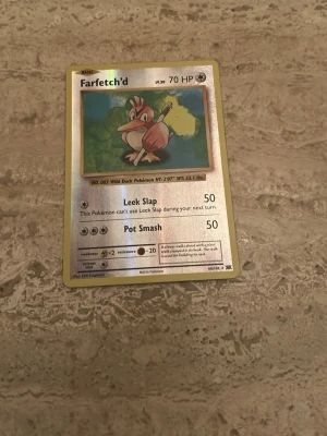 Farfetch’d Pokémonkort holo - Säljer ett holografiskt Farfetch’d Pokémonkort med 70 HP. Kortet har attacker som Leek Slap och Pot Smash. Framsidan har en glansig yta och baksidan har klassiskt blått Pokémon-motiv. Perfekt för samlare eller Pokémonfans.