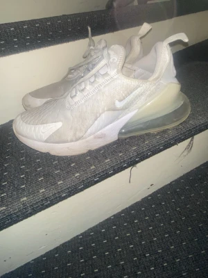 Nike Air Max 270 vita sneakers - Nike Air Max 270 sneakers i vitt med stora synliga Air Max-bubblor i hälen. Ovandelen är i mesh och syntetmaterial för bra andningsförmåga. Swoosh-logga på sidan och dragflik bak. Snygg, sportig design med chunky sula och tydliga detaljer.