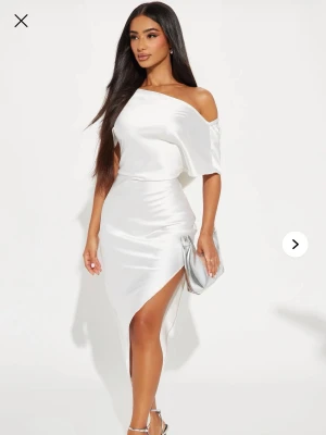 Student/bal klänning  - Helt ny och aldrig använd stilren vit oneshoulder klänning i tjockt, glansigt satinmaterial av bra kvalitet. Tjockt och bra material. Prislappen kvar och kommer i orderpåsen. Perfekt till studentmotagning exempelvis. 