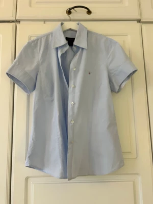 Ljusblå kortärmad skjorta från Gant💖💖💖 - Snygg ljusblå skjorta från Gant med korta ärmar och klassisk krage. Skjortan har knappar framtill och en liten broderad logga på bröstet. Perfekt till sommarens alla tillfällen och enkel att matcha med jeans eller shorts.